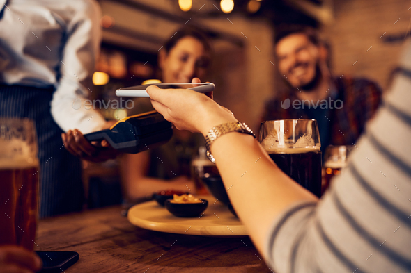 Close up of woman using cell phone while paying contactless in a pub. - Stock Photo - Images
