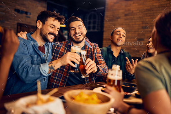 Happy men toasting while drinking beer with friends in bar. - Stock Photo - Images