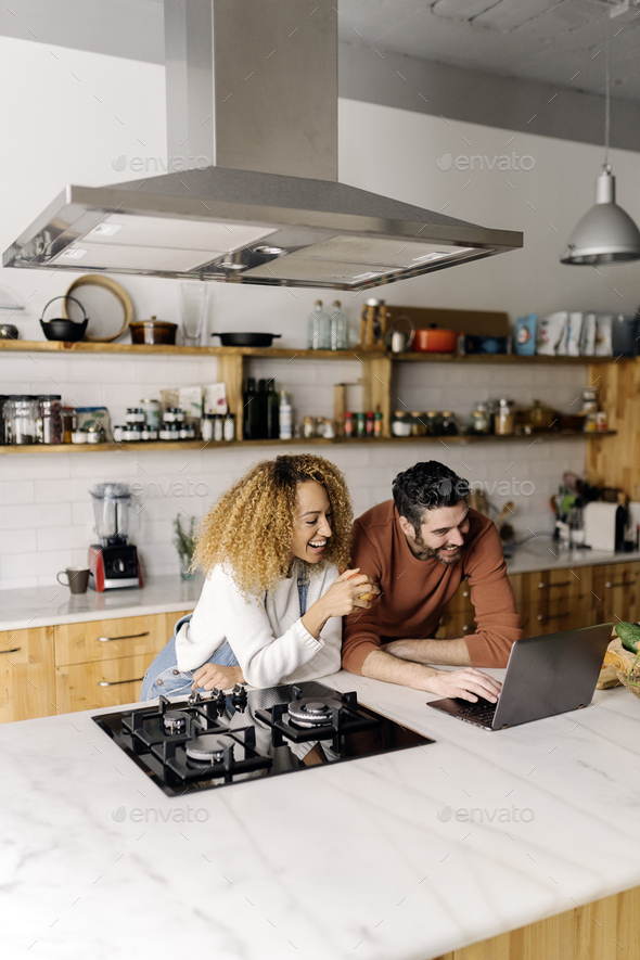 Couple looking at laptop in kitchen. - Stock Photo - Images