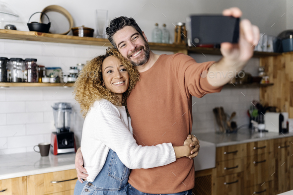 Couple taking a selfie standing in kitchen. - Stock Photo - Images