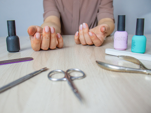 home manicure, woman saws her nails with a nail file, manicure tools and nail polish lie on the tab
