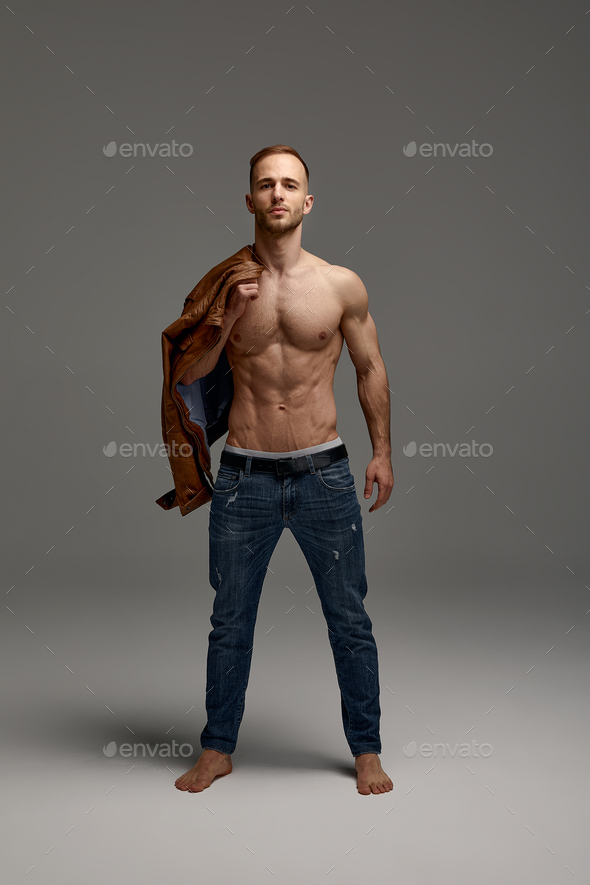 good looking male model posing with hands behind back in blue pants on gray  backdrop, fashion Stock Photo by LightFieldStudios