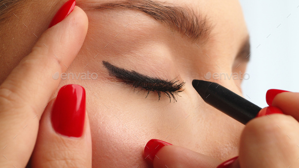 Closeup shot, stylist drawing black arrows on the eyes of the female model. Woman making make up.