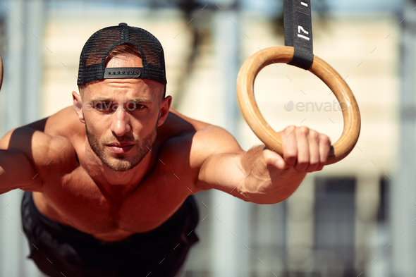 Muscular sportsman exercising on outdoor gymnastic rings in outdoor gym. Hands at rings dipping man