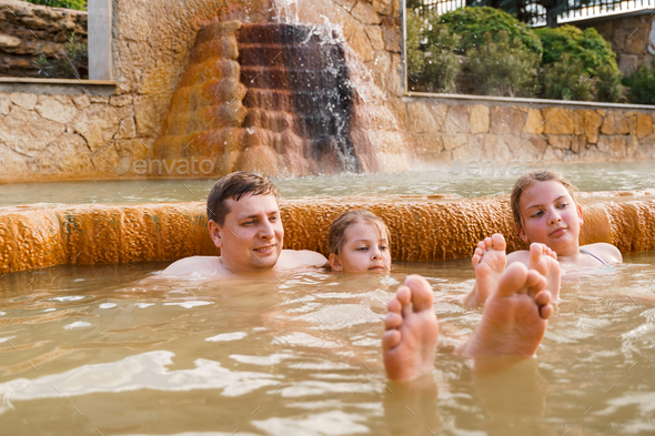 Family, dad and children bathe, swim in outdoor dirty hot springs. Thermal water bath pool and  - Stock Photo - Images