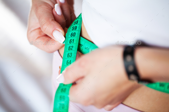 Slim young woman measuring her thin waist with a tape measure