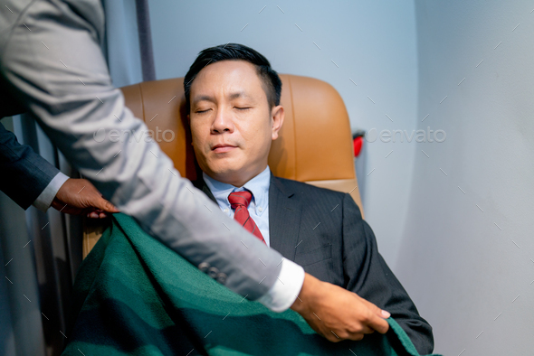 Airline staff help to cover the blanket to customer business man during flight for working.