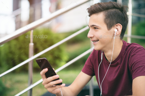 A smiling young man with a smartphone, in the street.  Happy teenage boy is using mobile phone.  - Stock Photo - Images