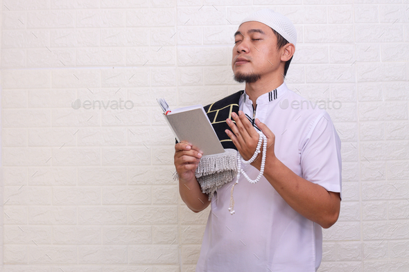 Asian Muslim man praying while holding the Quran and prayer beads - Stock Photo - Images