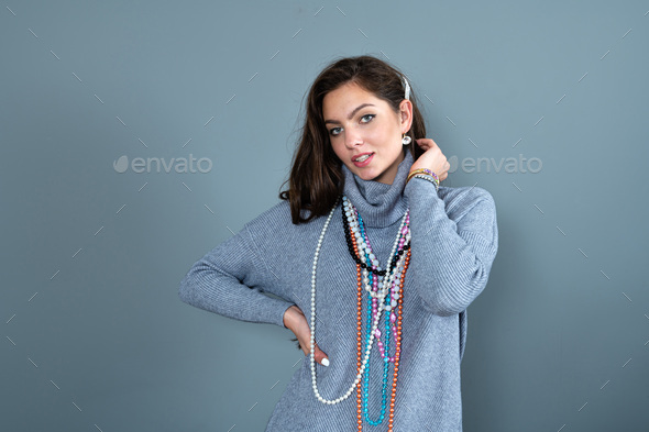 elegant woman in a long gray sweater has fun with many bead chains and jewelry, isolated on gray - Stock Photo - Images