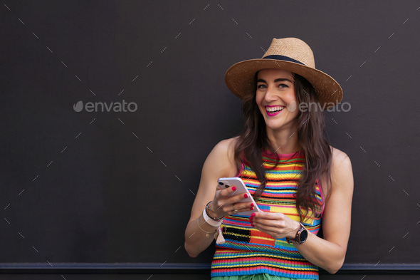 Smiling woman in hat and colorful t-shirt using smart phone. - Stock Photo - Images