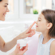 Cropped shot of affectionate young mum touches daughter`s nose, holds bottle of cream - PhotoDune Item for Sale