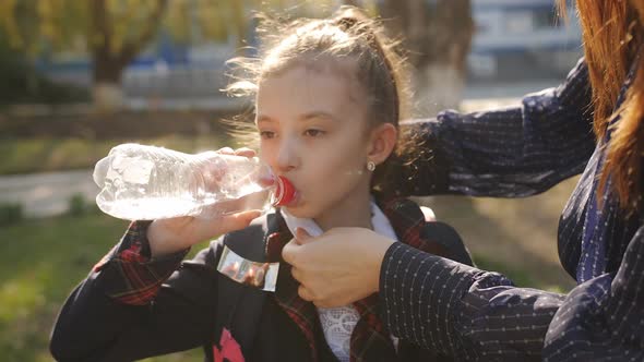 Little Girl in School Uniform Drinks Water From a Plastic Bottle