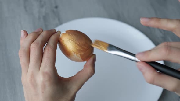 Close-up. Female hands paint Easter egg in a modern minimalist style with gold paint.