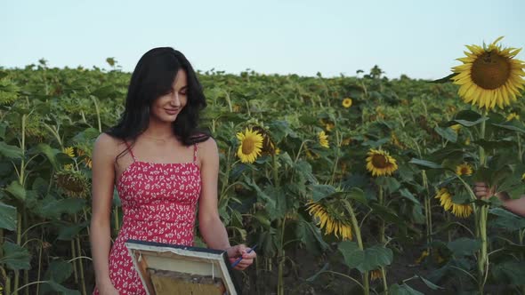 Handsome Man Comes and Presents Sunflower to His Painting Girl in Field alt