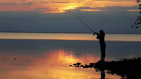 Woman Fishing on Fishing Rod Spinning at Sunset Background alt