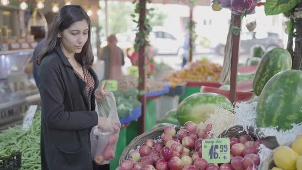 Young attractive woman shopping at the greengrocer choosing apple alt