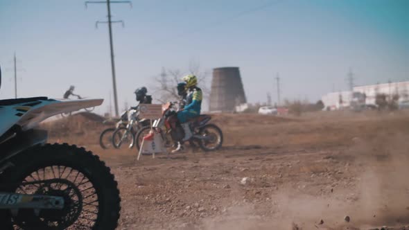 A motorcyclist drives along a sandy track past other riders.  Slow motion.