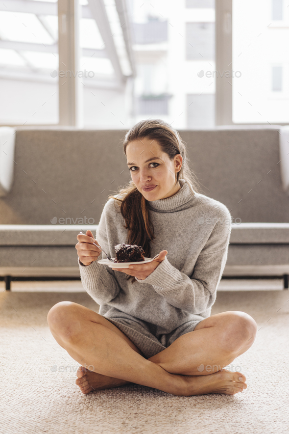 Portrait of woman sitting on floor eating piece of cake