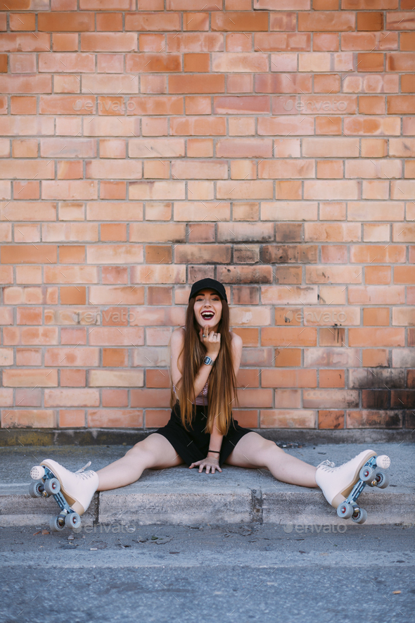 Portrait of laughing young woman with roller skates sitting on sidewalk Stock Photo by westend61