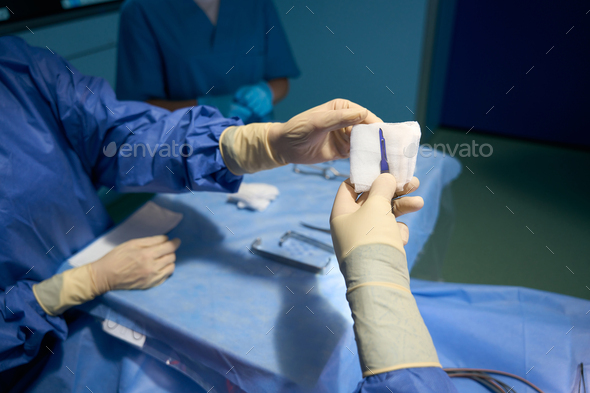 Assistant in the operating room passes the scalpel to surgeon