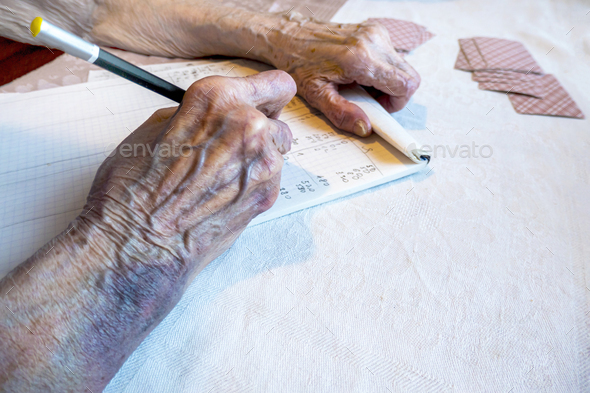 the hand of an elderly woman with bruises write the score in a card game