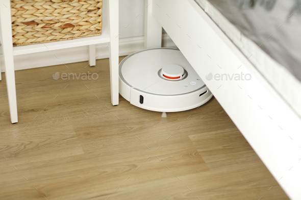 White robotic vacuum cleaner on laminate floor cleaning dust in living room interior. Smart electron