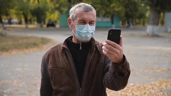 Senior Man Wearing a Medicinal Mask Talking on Video Chat with Their Children.