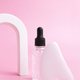 Glass bottle with oil, Gua sha stone for face massage on a pink background with arch. - PhotoDune Item for Sale