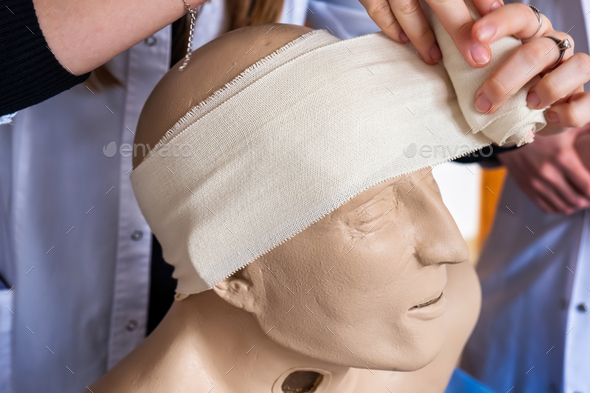 Hands of a medical doctor student learning how to put medical bandages on the head