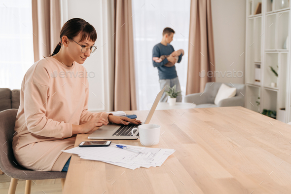 Busy parent mom using laptop for remote work while her husband is in paternity leave
