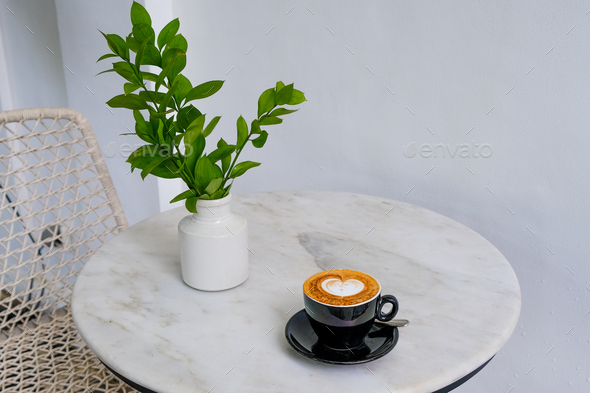 Black cup of tasty cappuccino with heart shaped latte art with vase with green leaves  - Stock Photo - Images