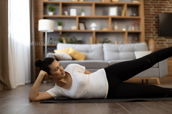 Multiethnic woman lying on yoga mat and lifting legs up