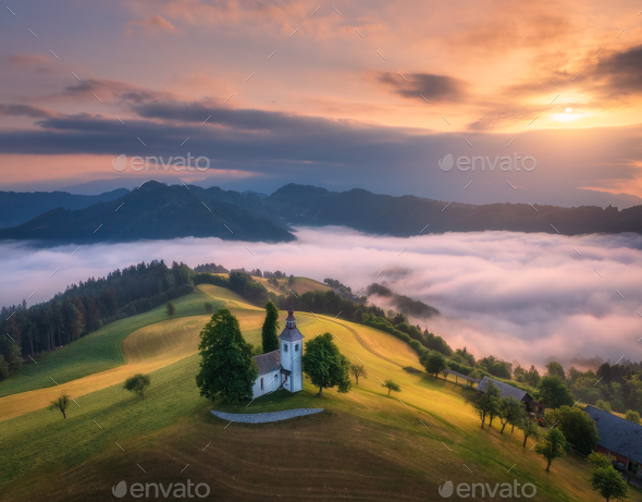Aerial view of small church on the hill over pink low clouds - Stock Photo - Images