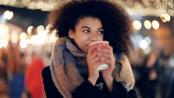 Woman standing at the evening street, drinking coffee