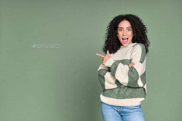 Young excited surprised latin woman pointing aside isolated on green. - Stock Photo - Images