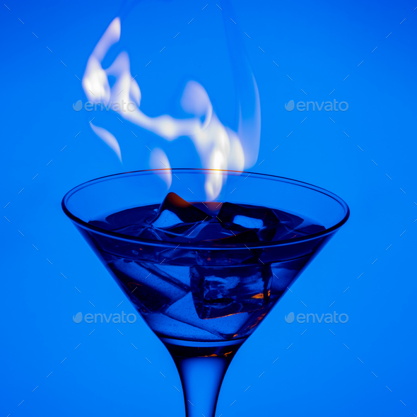 Burning alcoholic drink with ice cubes, on a blue background. Burning cocktail on table in a bar