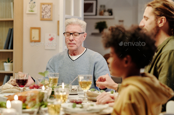 Focus on aged man with grey hair praying by served festive table - Stock Photo - Images