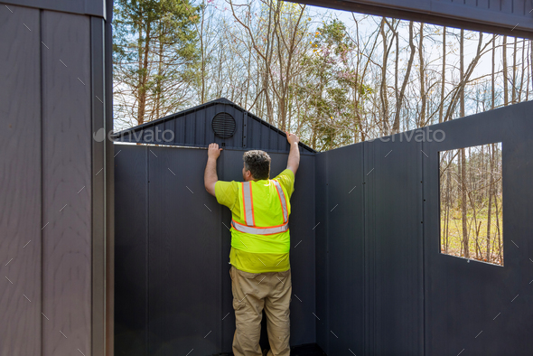 There is a worker assembling a plastic vinyl storage shed for a backyard near his house