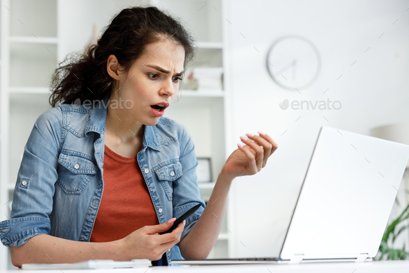 Disappointed girl looks at the laptop screen, does not understand what happened. Brunette woman is