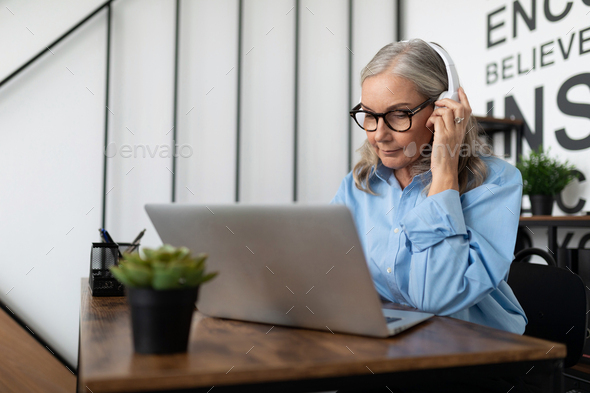 mature adult boss woman with gray hair has a conversation using internet and headset