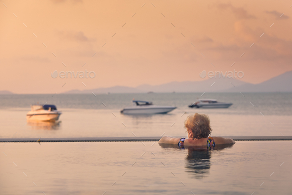 Active senior woman in swimming pool against sea at sunset - Stock Photo - Images