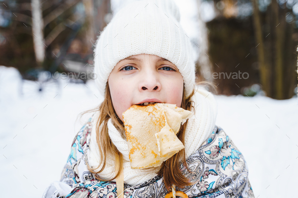 Russian national festival Maslenitsa, shrovetide. Little cute beautiful girls in headscarf eat big  - Stock Photo - Images