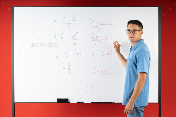 Serious young man wearing glasses, explaining math exercises on a white board, with a marker pen