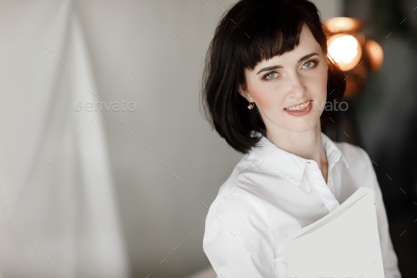 beautiful young woman with dark short hair holding a magazine, book with mock up. girl in a white