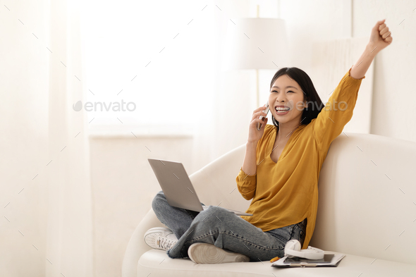 Emotional asian woman using laptop, have phone conversation, home interior - Stock Photo - Images
