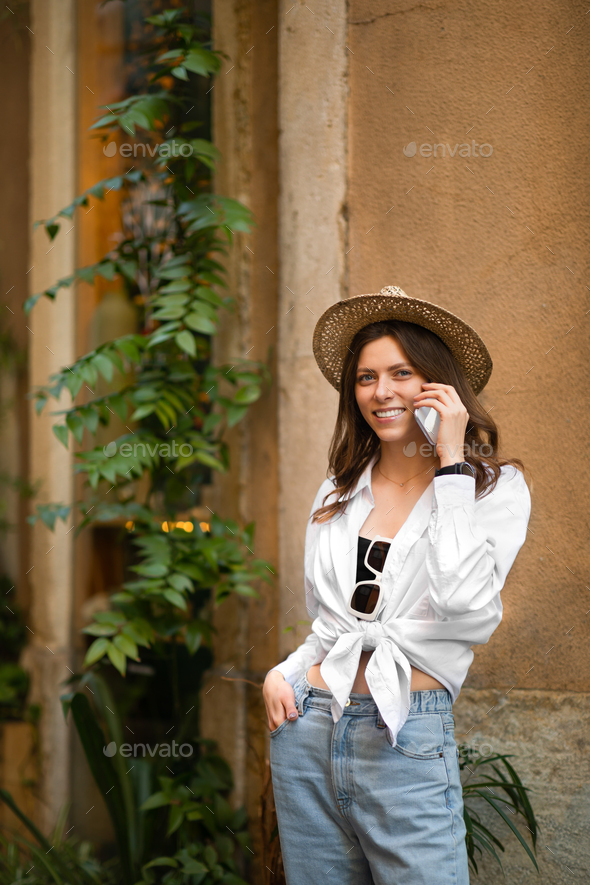 Glad young caucasian female in hat calling on smartphone looking at sights in city, outside - Stock Photo - Images