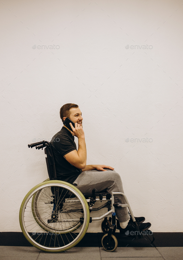 The disabled person sits in a wheelchair. He is talking to someone on