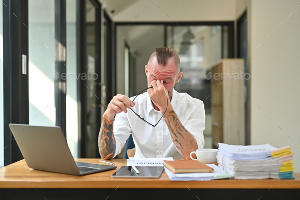 Frustrated young beard man holding glasses and rubbing nose