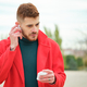 Latin young man with a red coat putting on wireless headphones. - PhotoDune Item for Sale